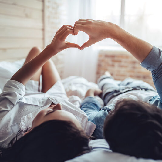 Beautiful young couple in bedroom is lying on bed. Enjoying spending time together.